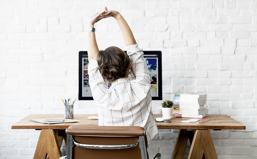 a woman sitting in front of a desk stretching her arms up
