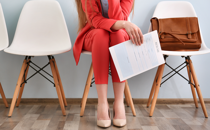 woman in a red suit sitting in a waiting room with a resume in her hand